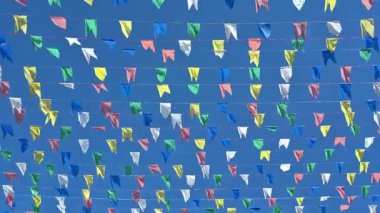 Açık mavi gökyüzüne karşı rüzgarda hareket eden ipe bağlanmış birkaç renkli bayrak.