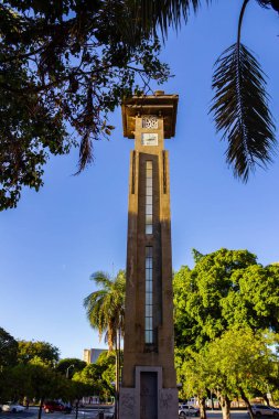 Goinia 'daki Avenida Gois' deki saat kulesinde ağaçların ve dalların detayları ve arka planda mavi bir gökyüzü var..