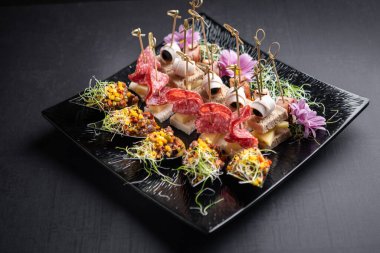 Çeşitli et türlerine sahip kanepeler peynirle ve mikroyeşille kompliman yapılıyor.