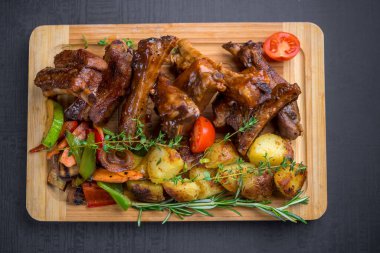 Kaburga manzarası. Patates, otlar ve ahşap tahtada servis edilen ızgara sebzelerle barbekü.