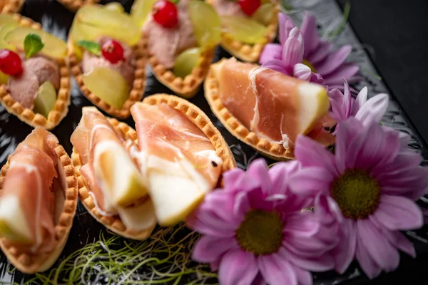 Canapes with prosciutto, berries and mashed vegetables served with flowers