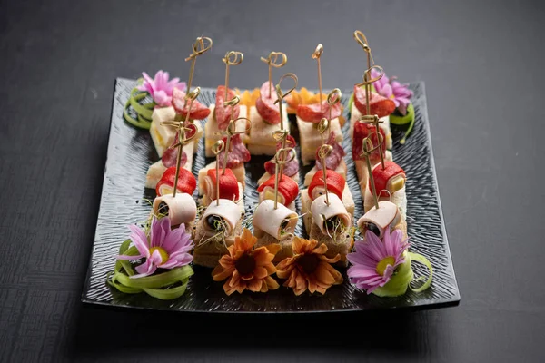 Jambonlu kanepeler, sosisler ve ahşap şişler ve çiçeklerle süslenmiş peynirler.