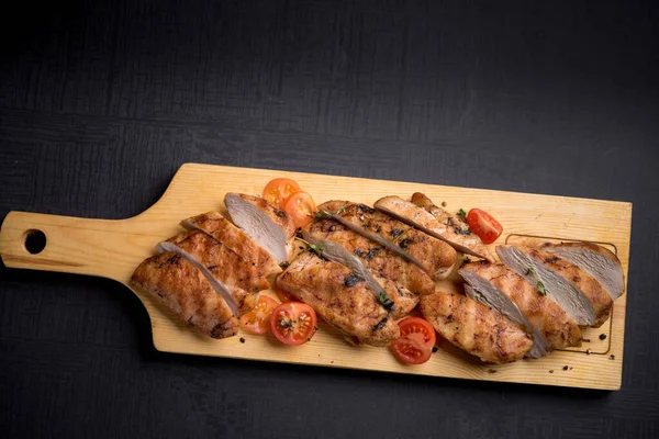Grilled chicken fillet with thyme and cherry tomatoes on wooden board