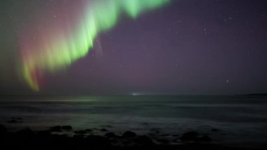 Active red and green aurora borealis over ocean waves open sky