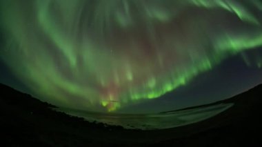 Full sky red and green aurora borealis over ocean waves