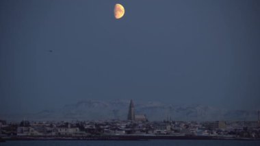 Kış boyunca Reykjavik üzerinde ay altında uçan helikopter.