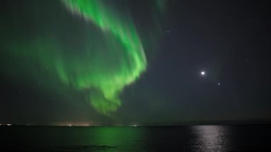 Parlak Aurora borealis Ay ve Venüs 'ün önündeki okyanusa yansıyor.