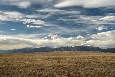 Bulutlar, Büyük Kum Tepeleri Ulusal Parkı 'nın arkasındaki kar örtülü dağların üzerinde toplanıyor.