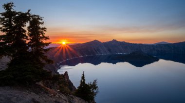 Orange Rays from Sunset Behind Mountains Over Crater Lake National Park