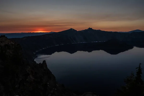 Dark Shadows Of Surrounding Cliffs Reflect In Crater Lake National Park