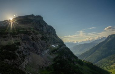 Late Day Sunburst Over Mount Overlin In Glacier clipart