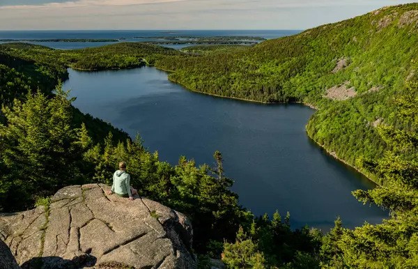 Acadia Ulusal Parkı 'ndaki Kartal Gölü' ne bakan Ledge 'de oturan kadın