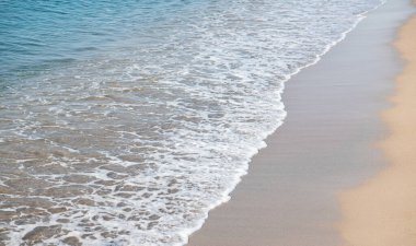 Kumlu sahilde yumuşak bir mavi deniz dalgası.