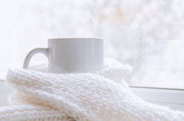 Bir kupa sıcak çay ve dışarıdaki kar manzarasına karşı cam kenarında yün örgü..
