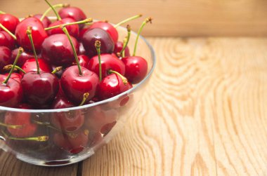 Kirazlar ahşap masada, su damlaları makro arka planda.