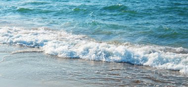 Kumlu sahilde yumuşak bir mavi deniz dalgası.