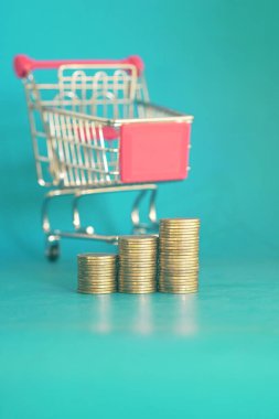 Mavi arka planda alışveriş arabasındaki altın sikkeler