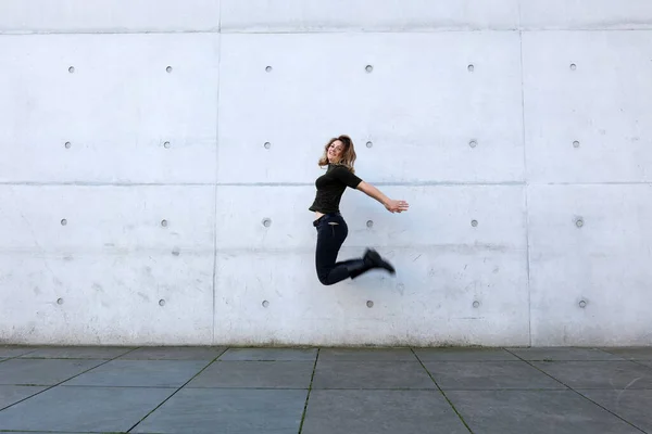 Молодая Женщина Черной Одежде Прыгает Перед Серой Стеной — стоковое фото