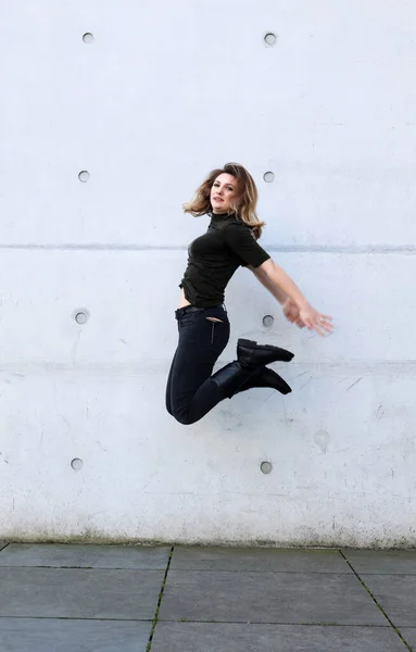 Young Woman Black Clothes Jumping Front Grey Wall Stock Photo