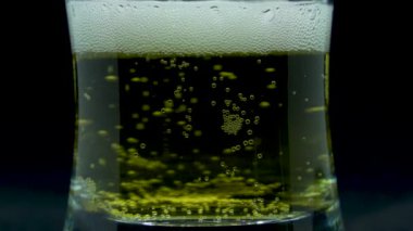 Soğuk bira köpükleriyle dolu şeffaf bir bardağın yakınlaştırılmış makro görüntüsü.