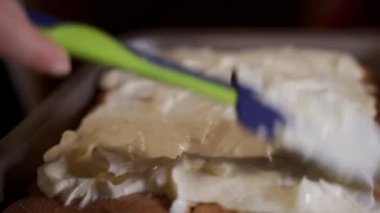 Extreme close up displaying a process of spreading cream made of raw whipped egg whites and mascarpone on tiramisu dessert.