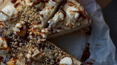 Close up of a creamy cheese cake with nuts and caramel topping being cut and served on a plate.