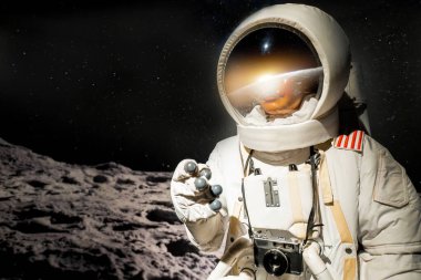 Boyuna kamera bağlanmış bir astronotun yakın çekimi. Uzay elbisesi ve dünyanın yansıması olan bir kask takıyor. Ve farklı bir gezegendeki güneş ışığı karanlıkta yıldızlara karşı.