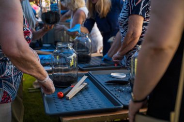 Bir grup insan, içinde toprak olan minyatür cam kavanoza tohum ekmek için atölyede bir araya geldiler. Seçici odak ve küçük alan derinliği