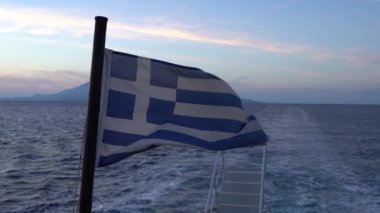 Dalgalı yırtık bir Yunan bayrağı, Akdeniz 'e karşı ağır çekimde rüzgarda dans ediyor