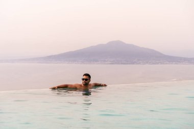 Bir erkek turist Campania İtalya 'daki Vezüv Dağı volkanına karşı havuzda eğleniyor ya da dinleniyor.