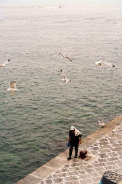 Sorrento, İtalya - 24 Temmuz 2024: Sisli bir günde etrafta martılar uçuşan bir adam Sorrento kıyısında yürüyor