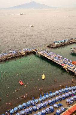 Sorrento, İtalya - 07.24.2019: İnsanlar iskelede plajda dinleniyor ve Sorrento 'daki şişme hava yataklarında denizde yüzüyor ve Vezüv Dağı' na karşı yüzen botlar