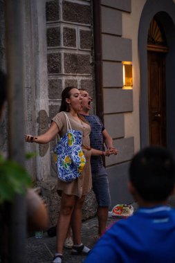 Sorrento, İtalya - 20 Haziran 2024: Büyüleyici bir sokak gösterisinde seyirci ve mimari arkaplan eşliğinde iki kişi tutkuyla opera söylüyor.