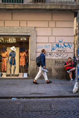 Napoli, İtalya - 22 Haziran 2024: Şehir vitrininin önünden şık mankenler ve kentsel graffiti ile geçen bir adamın gizli sahnesi. Yayalar modern şehir yaşamını ve gündelik modayı somutlaştırıyor..