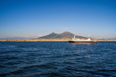 Napoli Körfezi 'nden görülen Vezüv Dağı' nın çarpıcı bir görüntüsü, ön planda seyreden bir gemi, doğanın ve denizcilik aktivitelerinin yan yana gelişini vurguluyor..