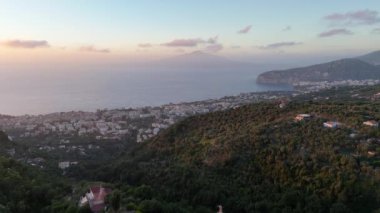 Akdeniz üzerindeki Vezüv Dağı 'na doğru yavaşça yaklaşan sinematik hava aracı Sorrento kasabasının üzerindeki günbatımında yeşil, Campania bölgesi, İtalya ve Avrupa ile çevrili.