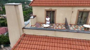 İtalya 'da bir adada deniz manzarasına karşı bir apartmanın balkonunda kahve içen bir adamın insansız hava aracı görüntüsü.