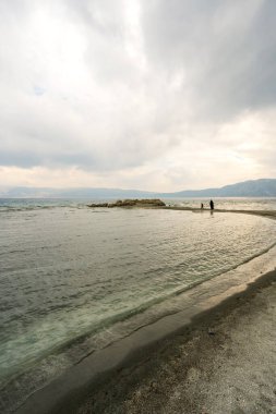 Türkiye 'nin Salda Gölü manzarası, el değmemiş beyaz kum ve turkuaz sularıyla hilal şeklinde bir koy sergiliyor. Tepemizde kara fırtına bulutları beliriyor. Sahneye dramatik bir dokunuş katıyor..