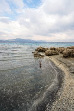 Turquoise waters and white mineral beaches of Lake Salda, Turkey, with a cloudy sky and rocky formations in the background. clipart