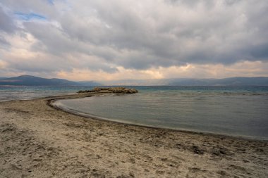 Türkiye 'nin Salda Gölü' nde sakin bir manzara, kumlu bir sahil, uzaklığa, berrak sulara ve bulutlu bir gökyüzünün altındaki dağlara doğru kıvrılıyor..