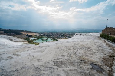 Pamukkale 'nin eşsiz jeolojik oluşumlarına ve Türkiye' nin yakınlarındaki bir kasabaya çarpıcı geniş bir bakış açısı, dramatik bulutlara karşı doğal güzelliği ve büyüleyici manzarayı gözler önüne seriyor.