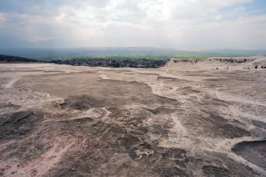 Kırmızı, kahverengi ve sarı tonlarda mineral çökeltilerinin sığ su havuzlarıyla vurgulandığı daha geniş bir arazi manzarası..