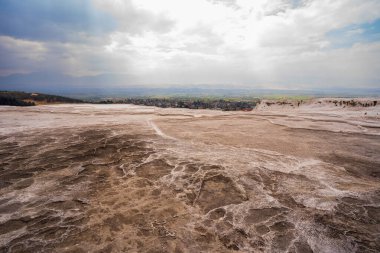 Kırmızı, kahverengi ve sarı tonlarda mineral çökeltilerinin sığ su havuzlarıyla vurgulandığı daha geniş bir arazi manzarası..