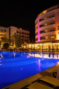Alanya, Türkiye - 17 Eylül 2021: Türkiye 'nin Antalya kentindeki şezlonglar ve palmiye ağaçlarıyla çevrili güzel aydınlatılmış bir otel havuzu.