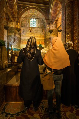 Konya, Türkiye - 14 Eylül 2021: Geleneksel başörtüsü takan üç kadın, kültürel ve dini önemi karmaşık mimari ayrıntılarla vurgulayarak, güzel dekore edilmiş tarihi bir caminin içinde duruyor.