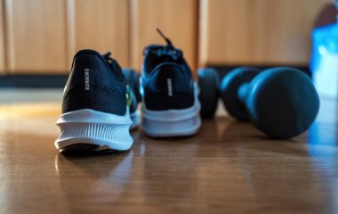 Bir çift siyah koşu ayakkabısını ahşap bir zemindeki dambılların önüne yerleştirin, ev antrenmanında spor ve spor malzemelerini gösterin..