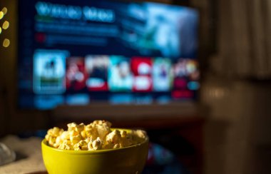 A bowl of popcorn in the foreground with a TV in the background showing a streaming service interface. clipart