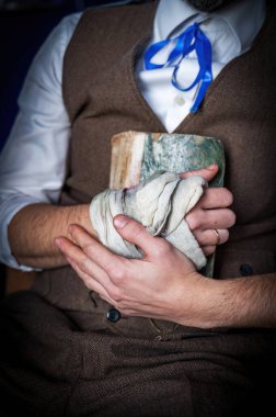 A close-up of a man's hands holding an old, well-loved book. His left hand is bandaged, suggesting a recent injury. clipart