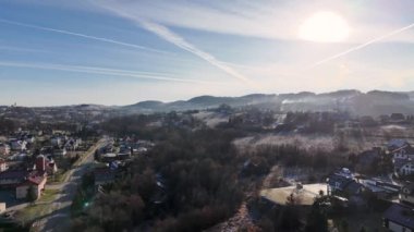 Gün batımında yuvarlanan tepelerin arasına yerleşmiş Polonyalı bir kasabanın nefes kesici hava manzarası. Güneş ufkun altına batarken gökyüzü canlı renklerle parlıyor..