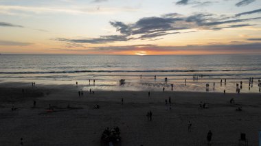 Bali sahilinde sakin bir günbatımı. İnsanlar manzaranın tadını çıkarıyor ve sahilde yürüyor. Islak kumda gökyüzünün renklerini yansıtıyor..